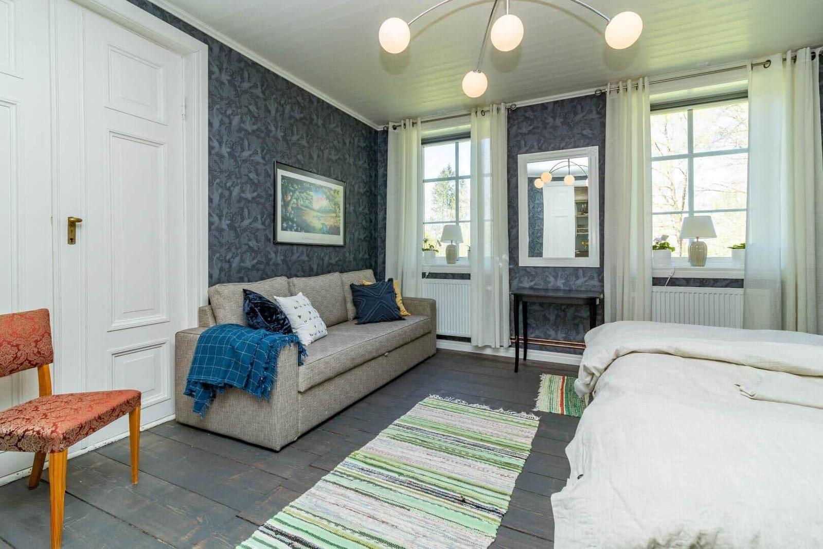 Zimmer mit Sofa, Bett und Fenstern. Wandtapete, Teppich und Decke.