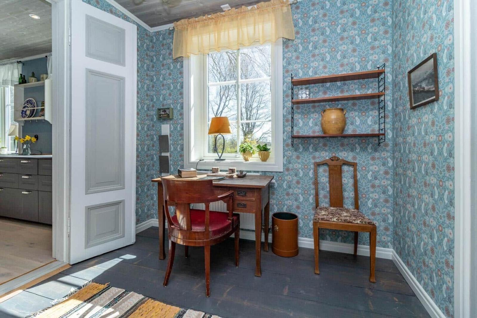 Ein Arbeitszimmer mit Holzschreibtisch, zwei Stühlen und floraler Tapete an den Wänden.