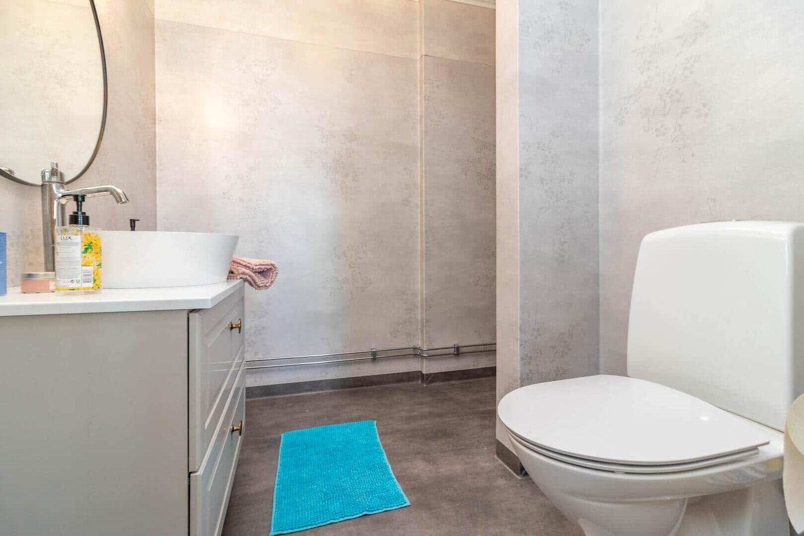 Badezimmer mit Waschbecken, Toilette und Dusche. Blauer Teppich auf dem Boden.