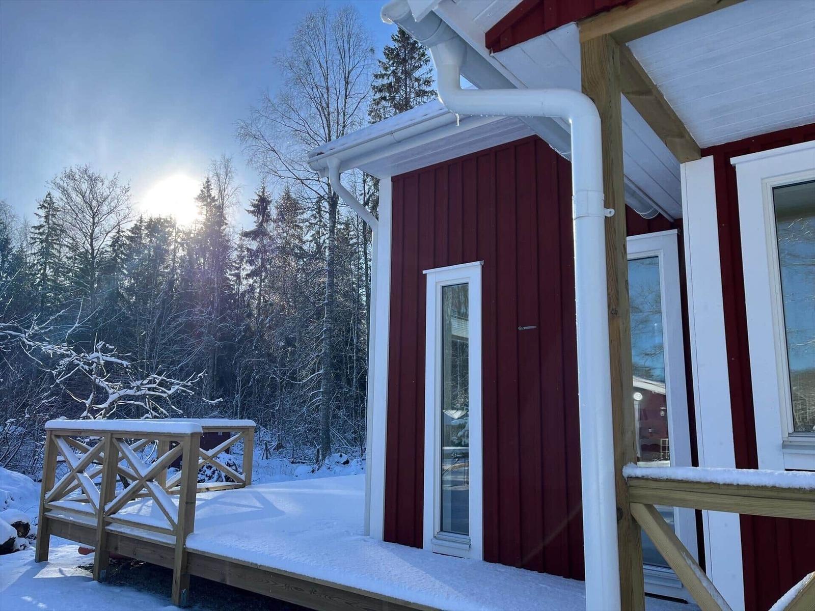 Rotes Haus mit Schneebedeckter Terrasse und Wald im Hintergrund.
