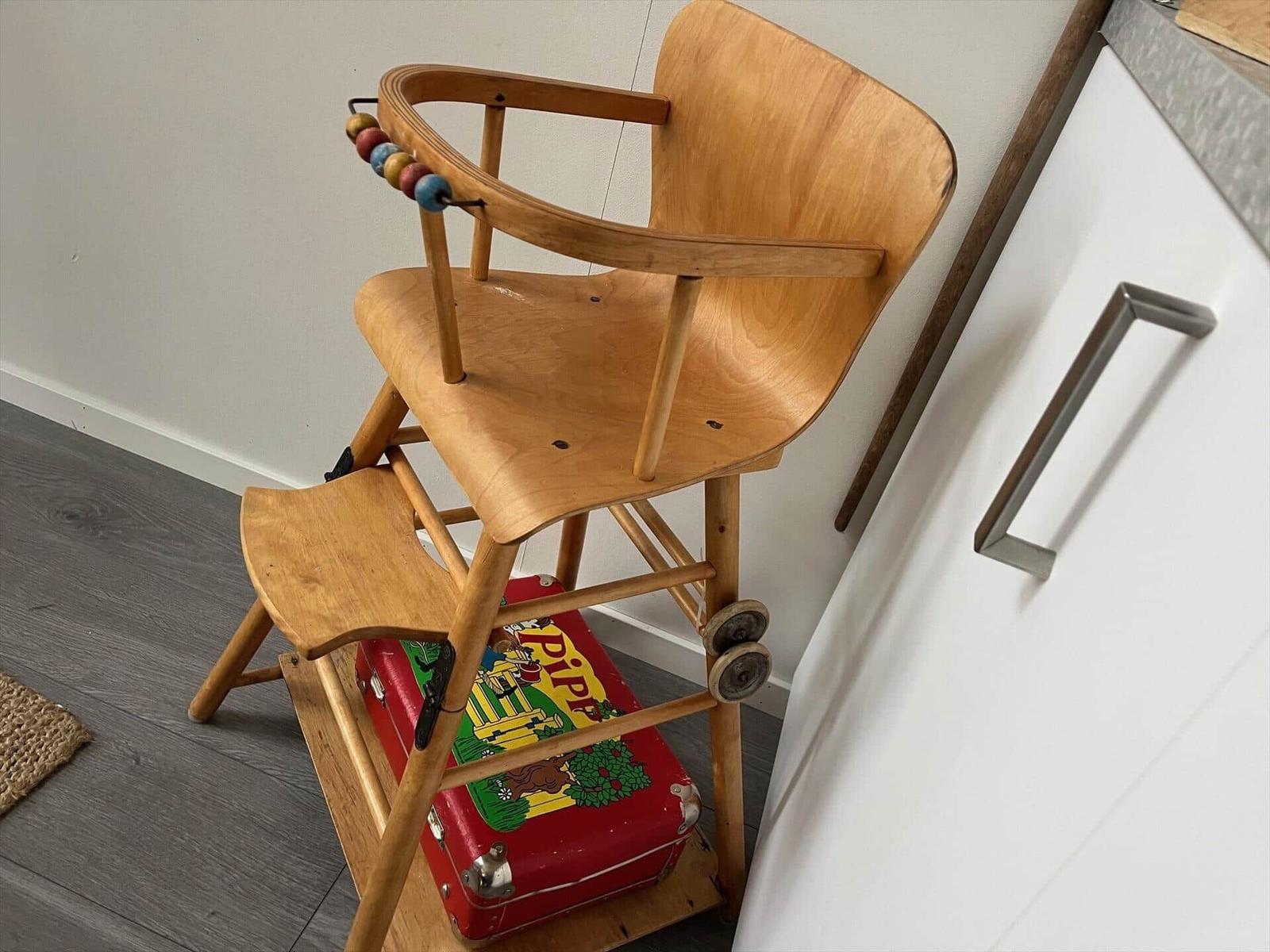 Holz-Hochstuhl mit bunten Perlen und roter Kiste darunter.