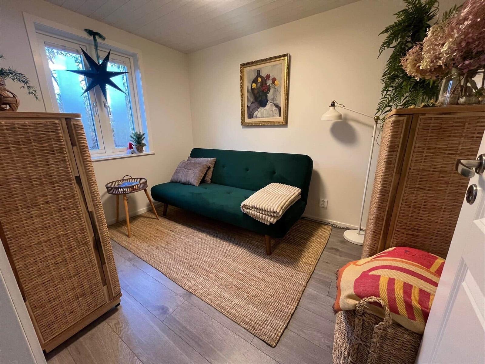 Ein Wohnraum mit grünem Sofa, Teppich und wicker Möbeln. Fenster und Wandbild sind sichtbar.