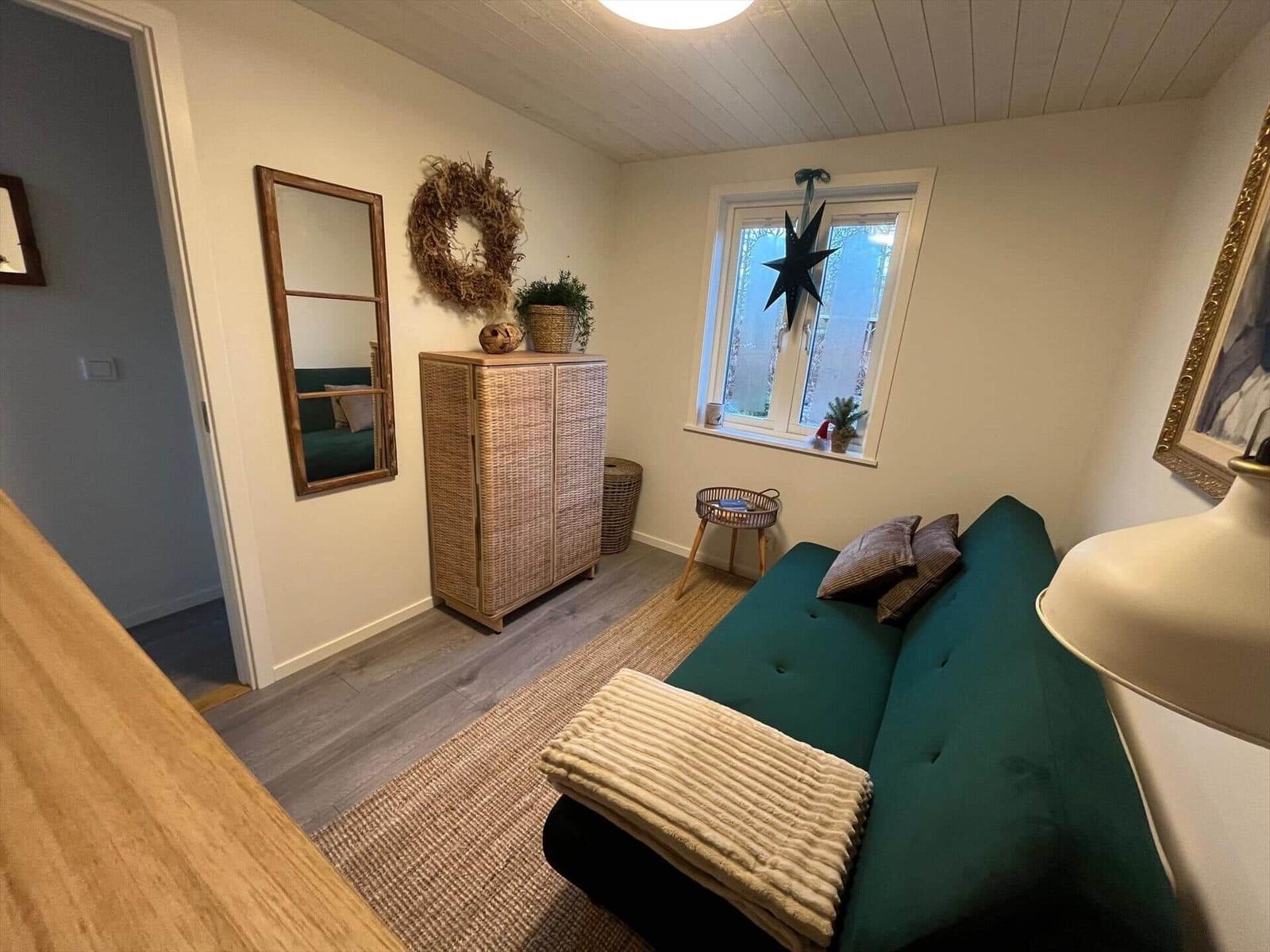 Ein Wohnzimmer mit grünem Sofa, Korbregal und Fenster mit Stern. Holzboden und Wandspiegel.