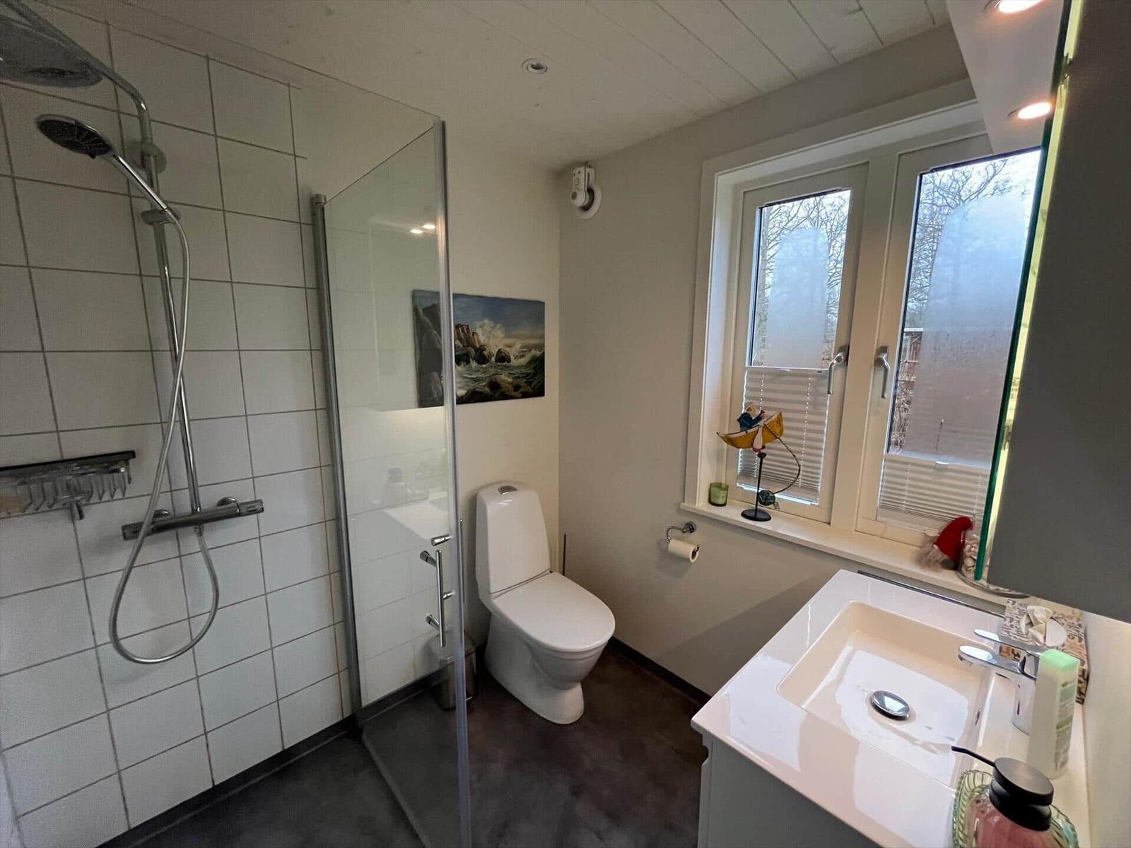 Badezimmer mit Dusche, Toilette und Waschbecken. Fenster mit Jalousie und Wandbild.