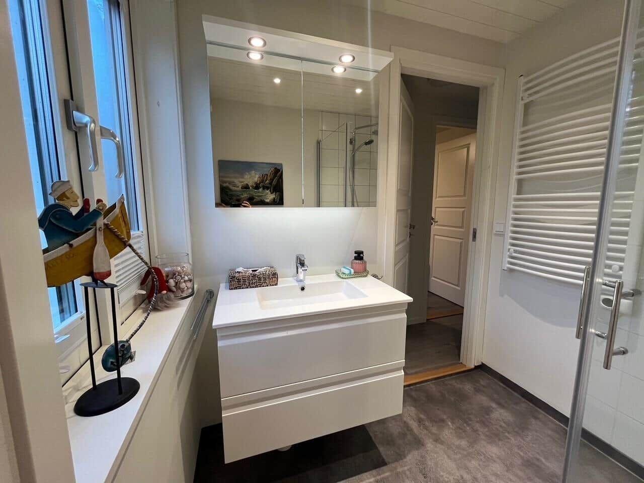 Badezimmer mit Waschbecken, Spiegel und Dusche. Fenster mit Segelboot-Dekoration.