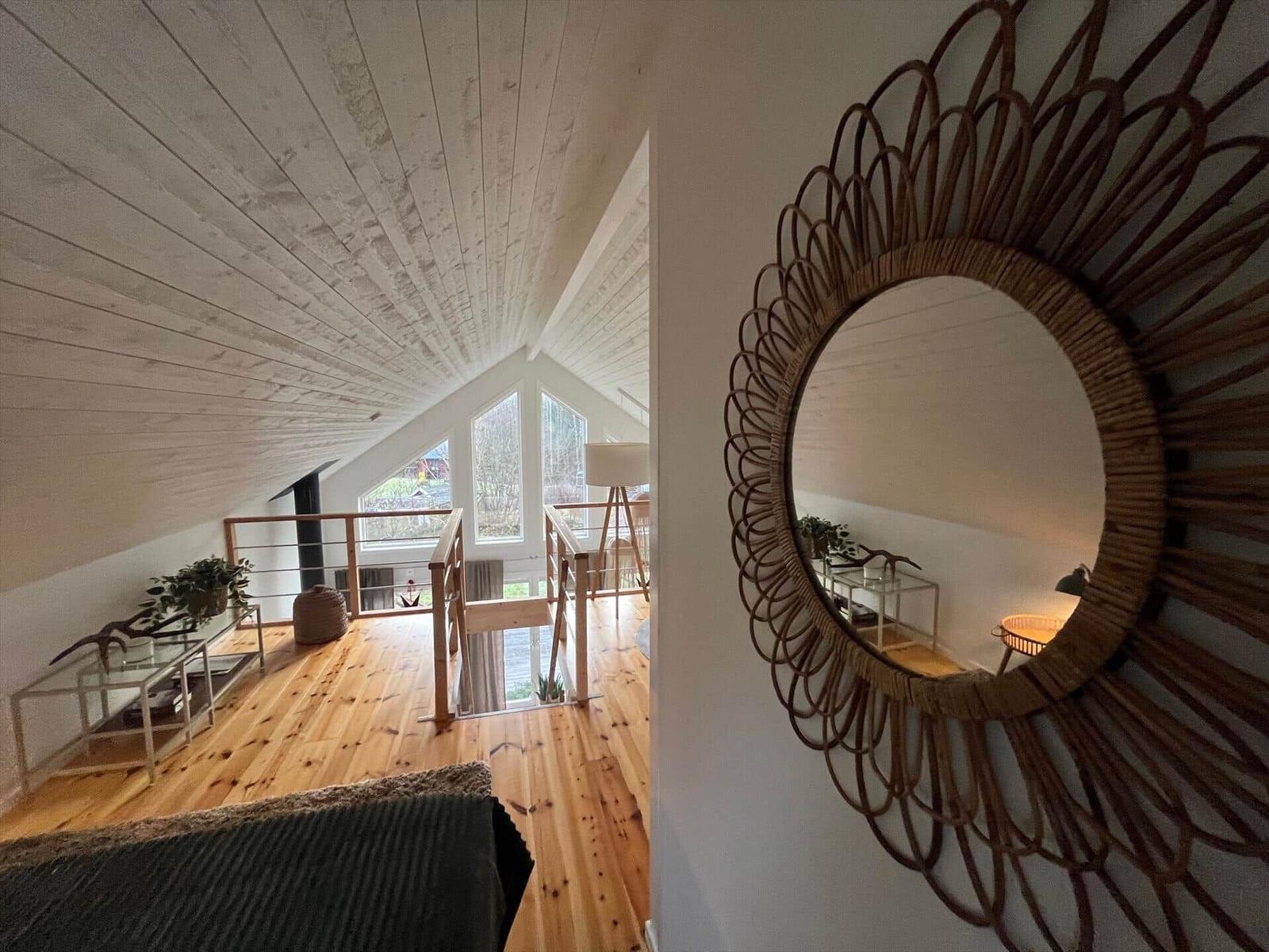 Wohnbereich mit Holzboden, Dachschrägen und Rattan-Spiegel an der Wand.