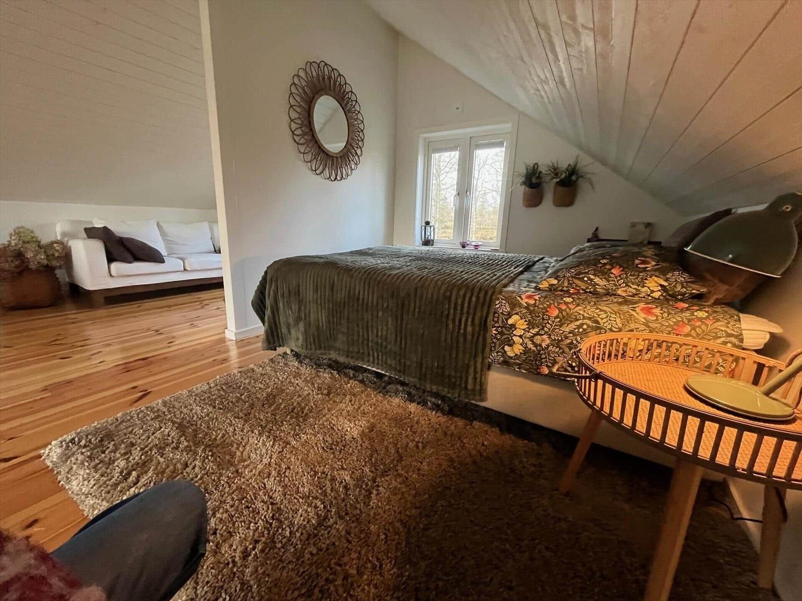 Schlafzimmer mit Bett, Teppich und Sitzgelegenheit. Holzboden und Dachschrägen.