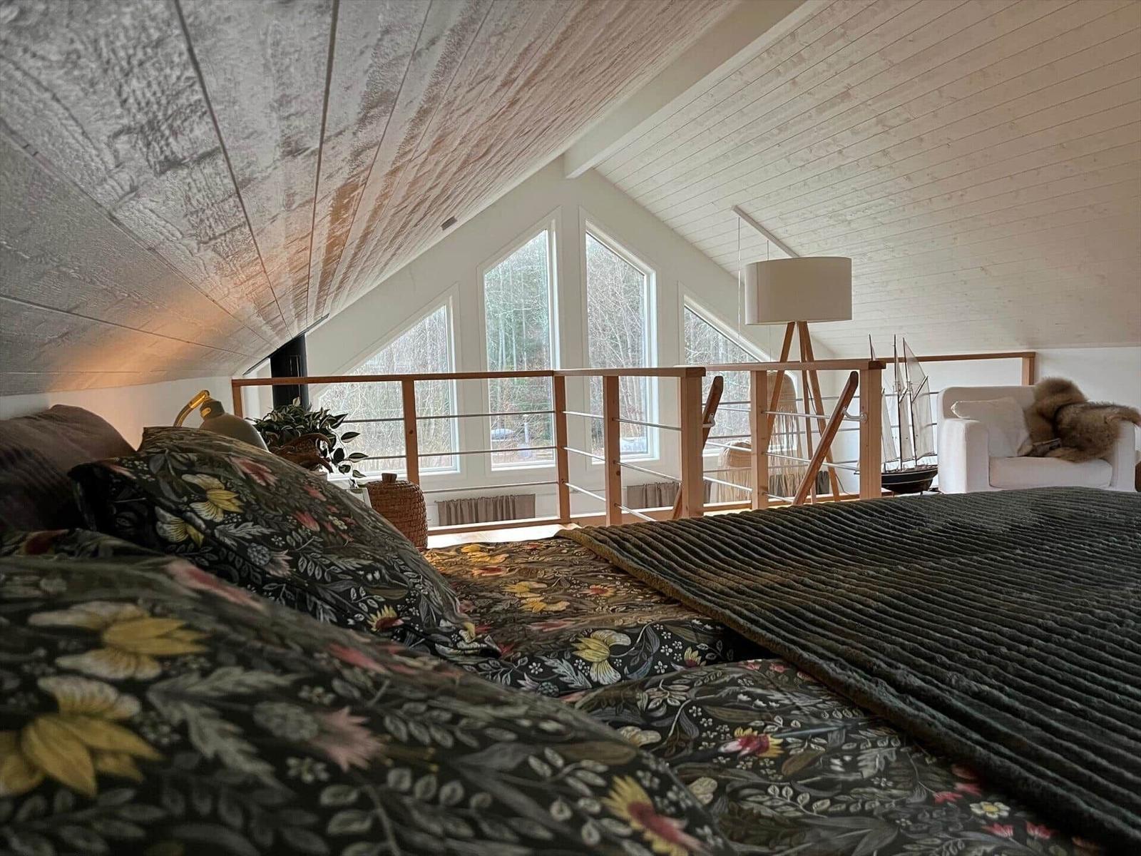 Schlafzimmer mit Blick auf Balkon und Fenster. Holzdecke und Bett mit floraler Bettwäsche.