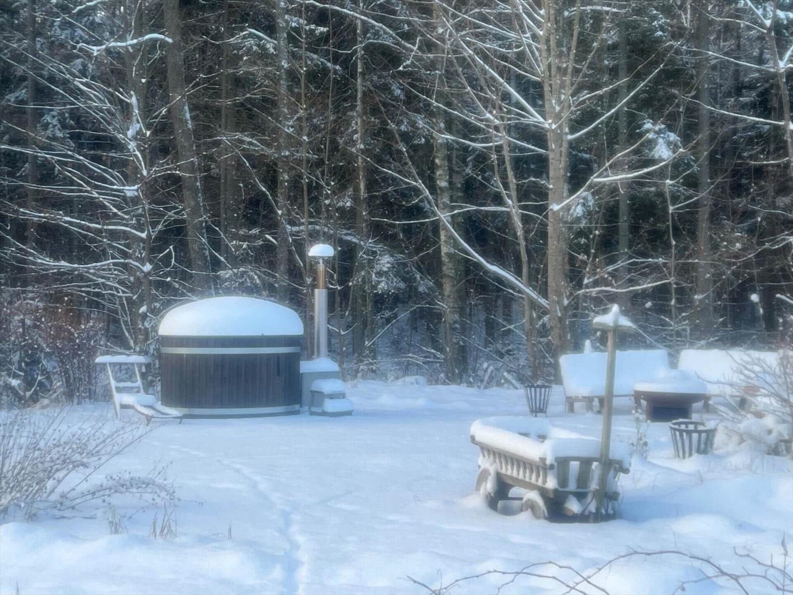 Schneebedeckter Hot Tub im Wald mit Gartenmöbeln und Bäumen.