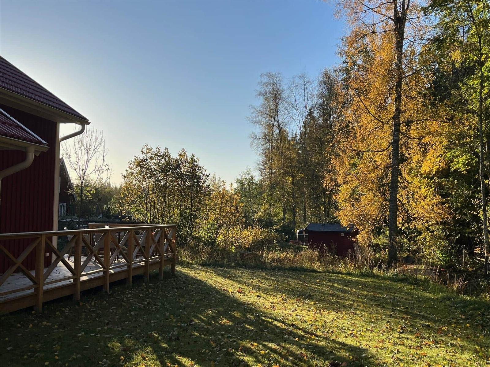 Roter Holzhaus mit Terrasse, umgeben von Herbstbäumen und Grasfläche.