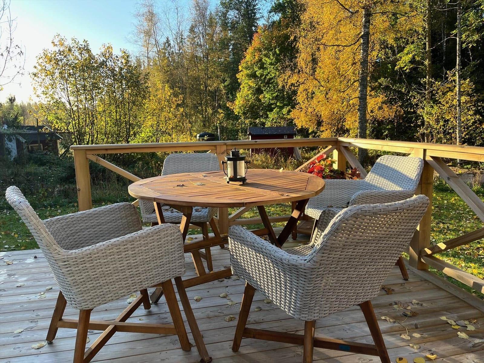 Terrasse mit runden Tisch und vier Stühlen, umgeben von Herbstlaub und Wald.