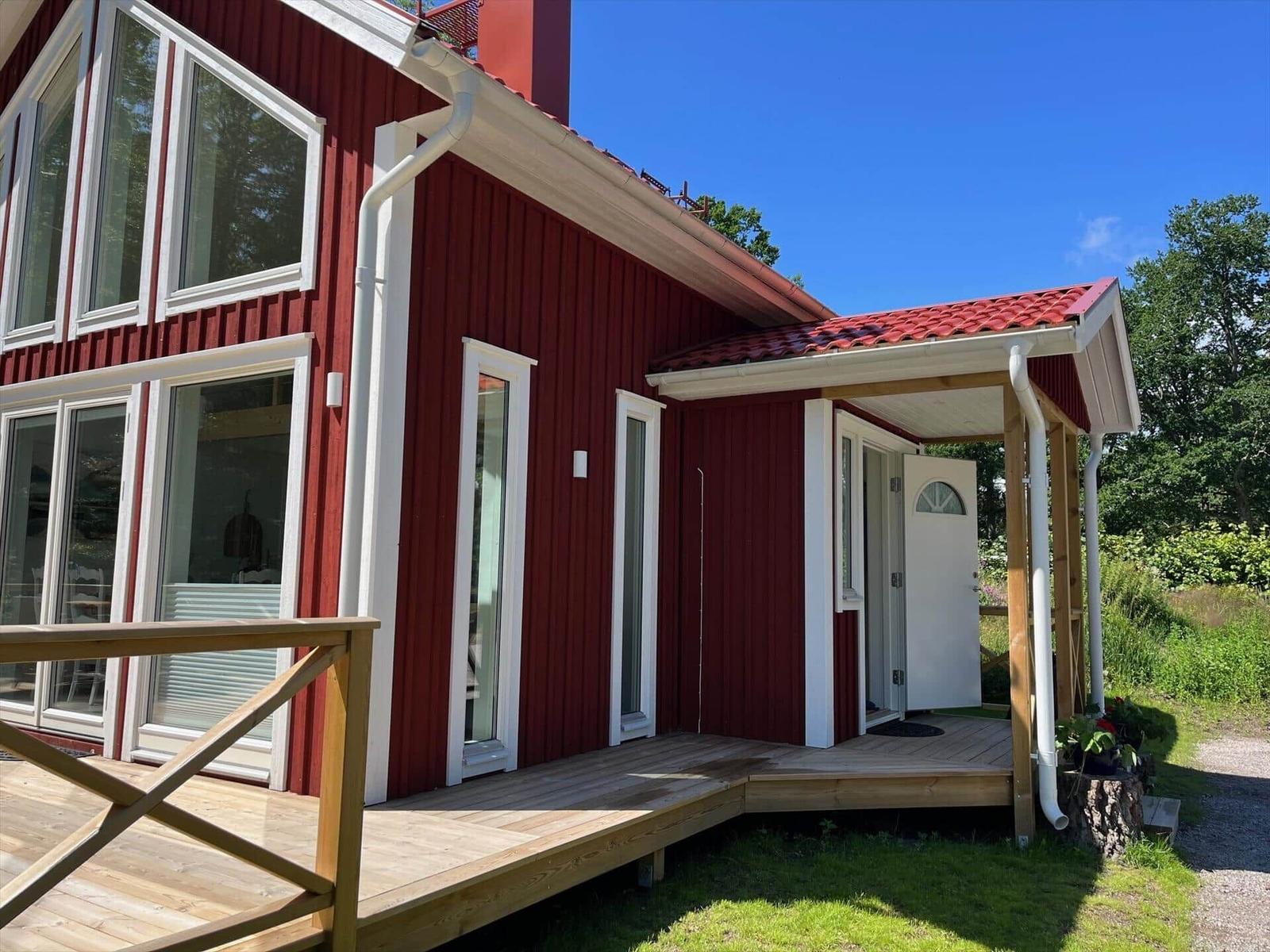 Rotes Holzhaus mit Terrasse und weißer Tür unter blauem Himmel.