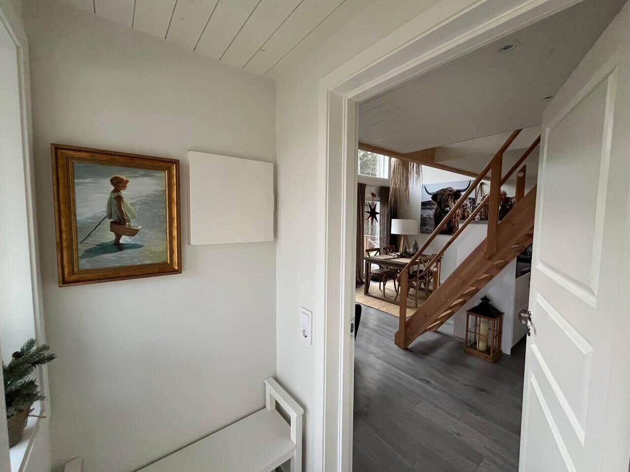 Hausgang mit Bild an der Wand, Blick in Wohnbereich mit Holztreppe und Tisch.