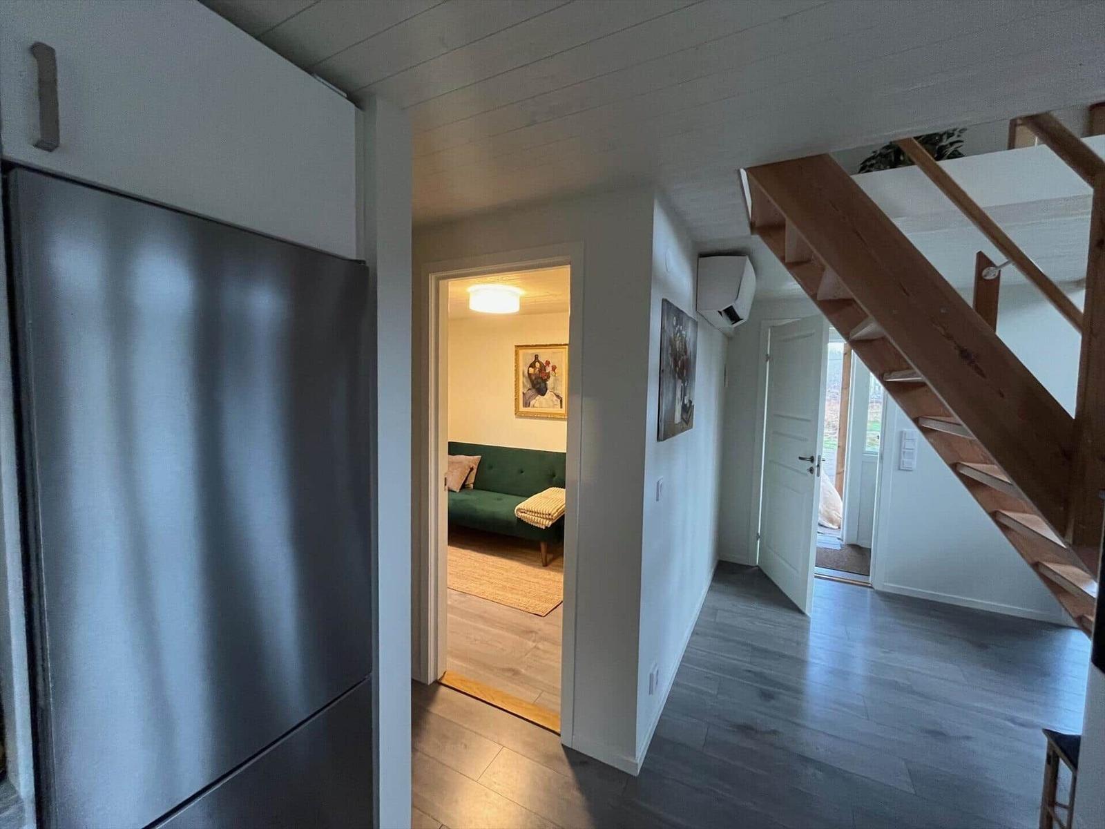 Küche mit Kühlschrank, Flur mit Holztreppe und Blick in Wohnzimmer mit Sofa.
