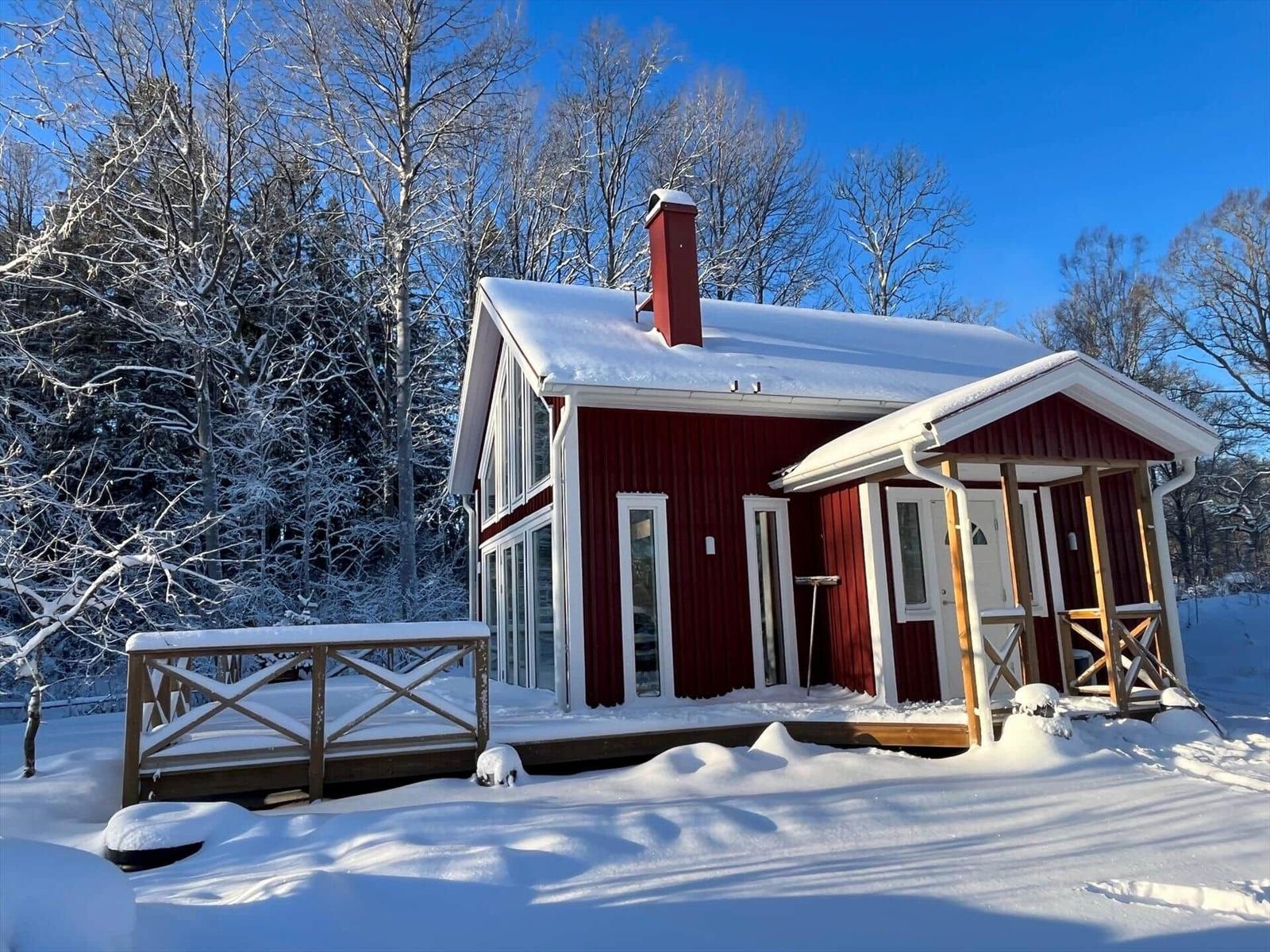 Rotes Holzhaus mit Schneebedecktem Dach und Terrasse im Wald.