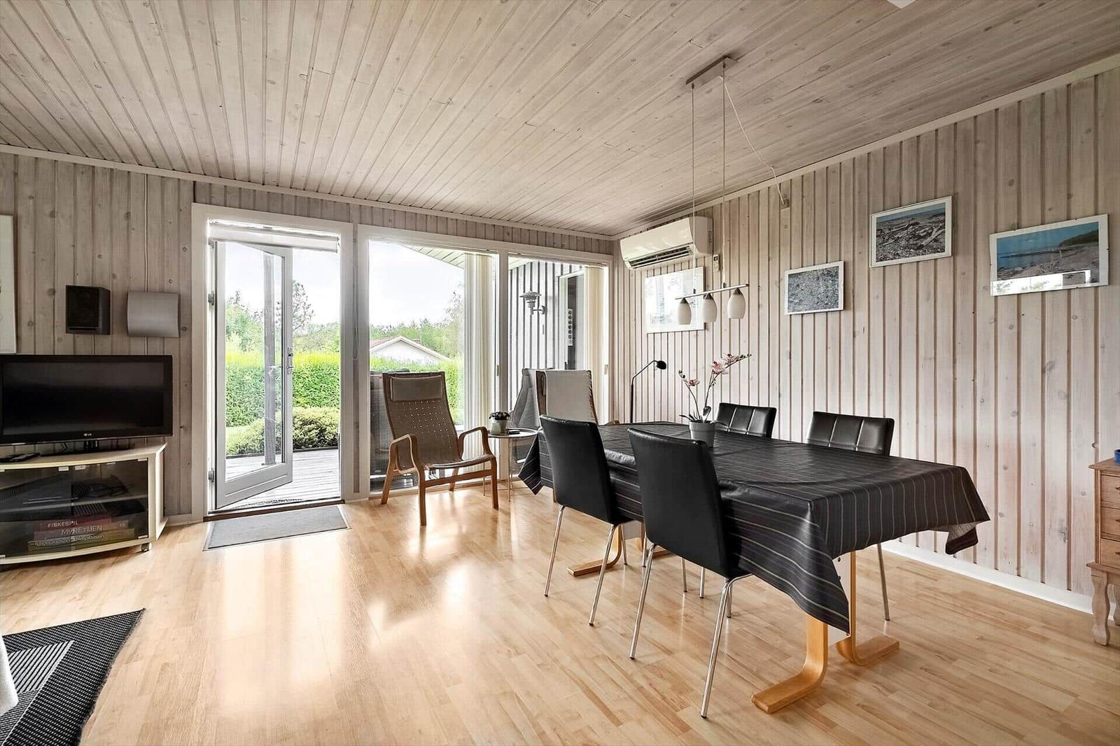 Esszimmer mit Tisch, Stühlen und Holzboden. Durchgang zur Terrasse mit Sitzgelegenheiten.
