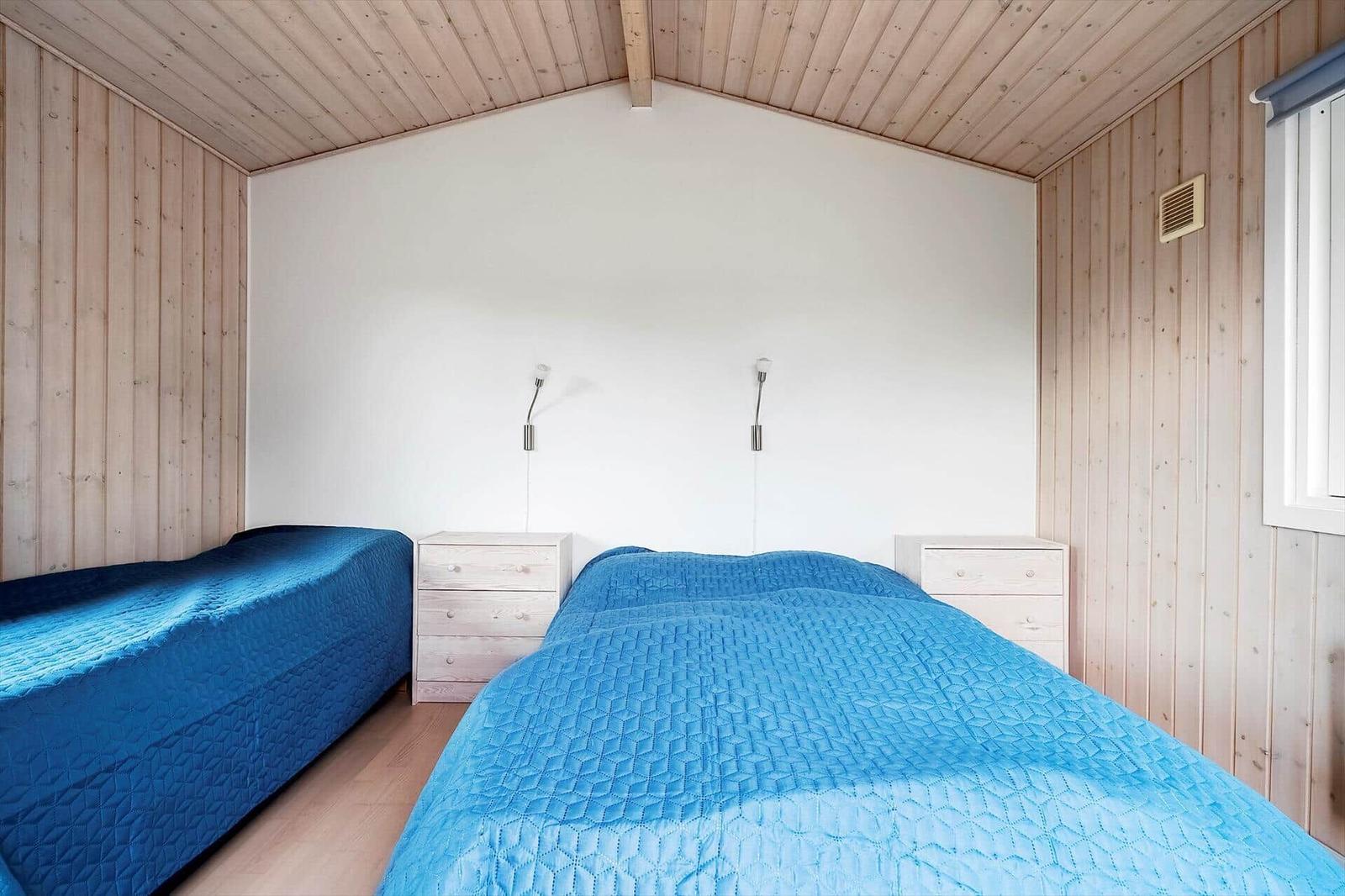 Zwei Betten mit blauen Bettdecken, Nachttische und Wandlampen in einem Holzhauszimmer.