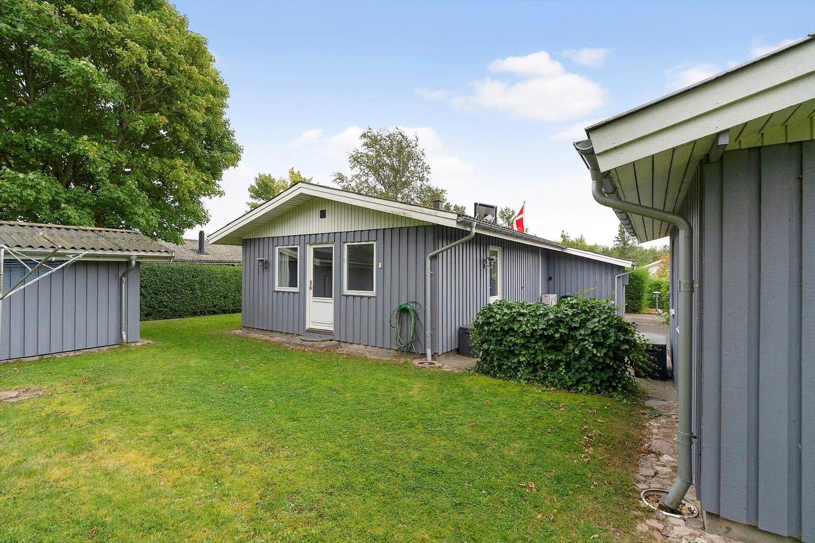 Ein graues Haus mit Garten und Flagge. Neben einem kleinen Schuppen.