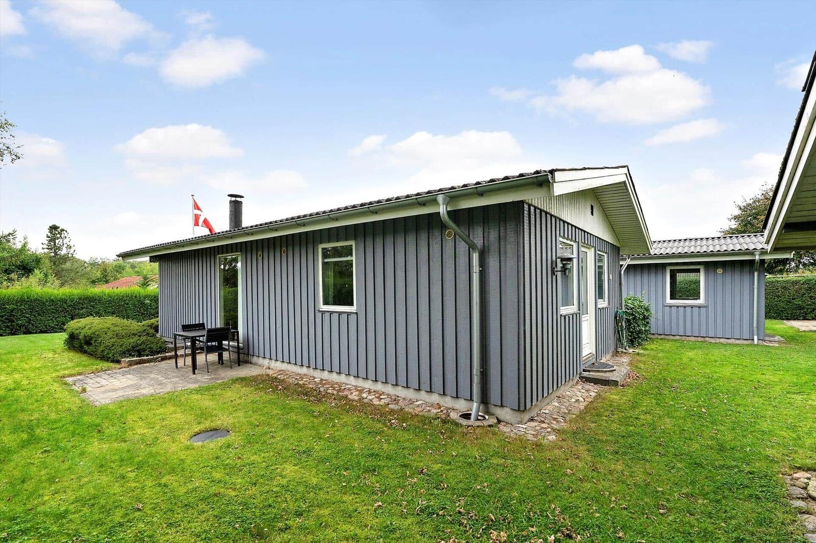 Ein graues Holzhaus mit Garten und Terrasse unter blauem Himmel.