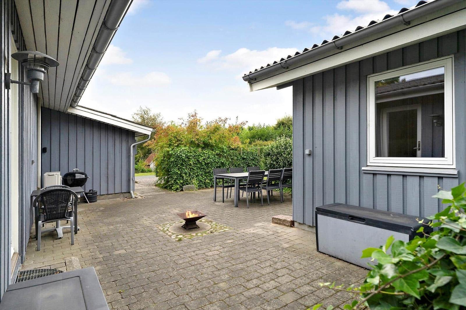 Terrasse mit Grill, Sitzgruppe und Feuerkorb. Umgeben von grüner Vegetation.