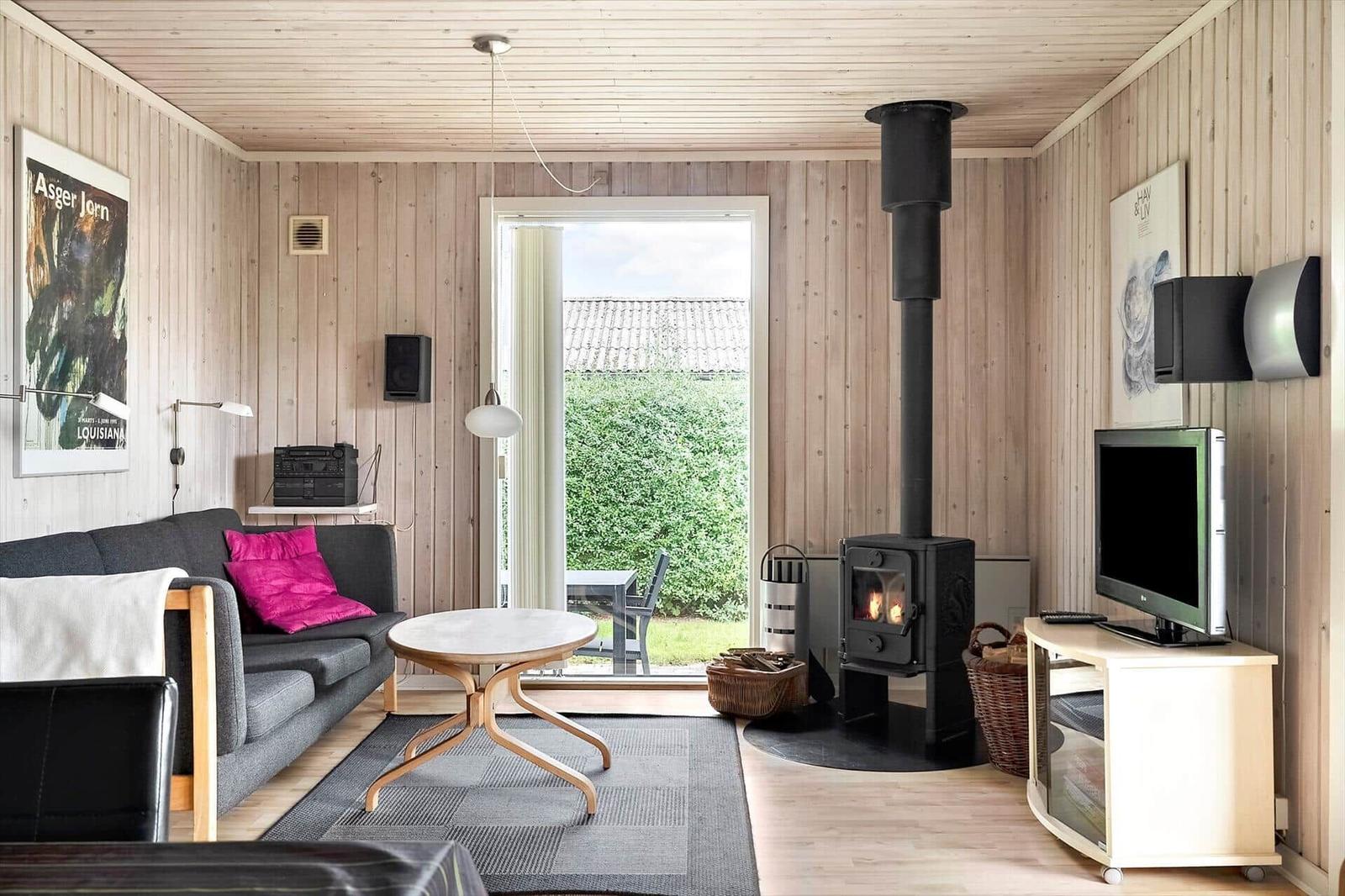 Wohnzimmer mit Holzwand, Kaminofen, Sofa und Fernseher. Durchgang zur Terrasse.