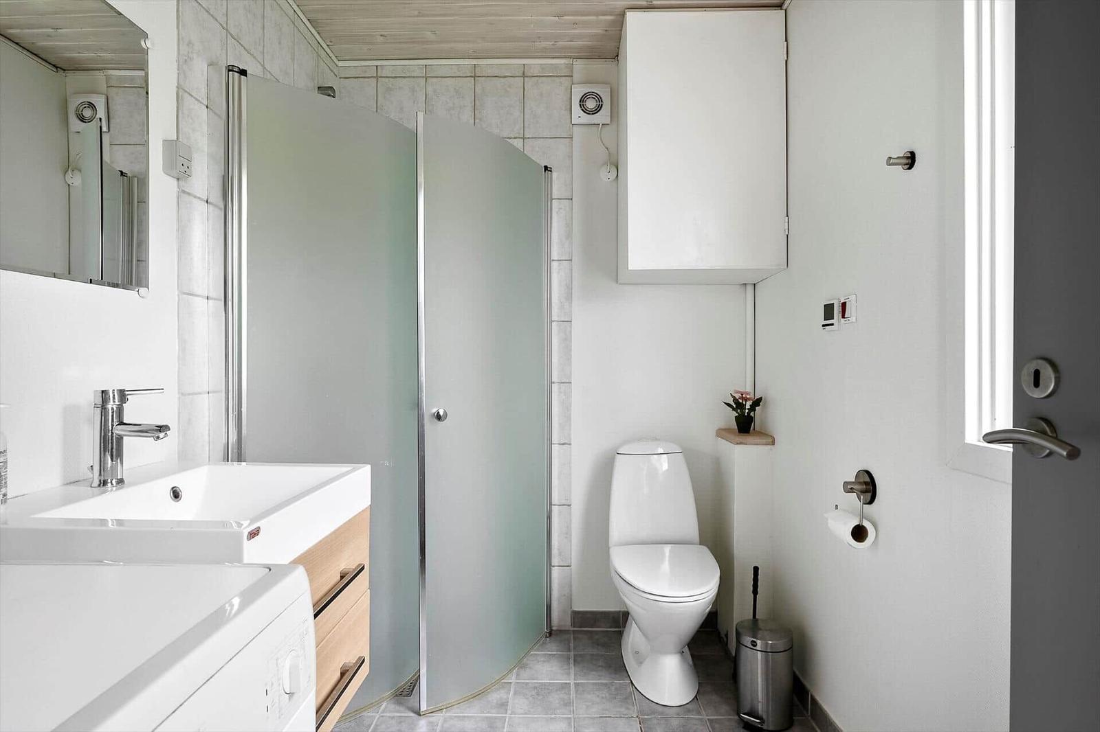 Badezimmer mit Dusche, Waschbecken und Toilette. Fenster und Spiegel sorgen für Tageslicht.