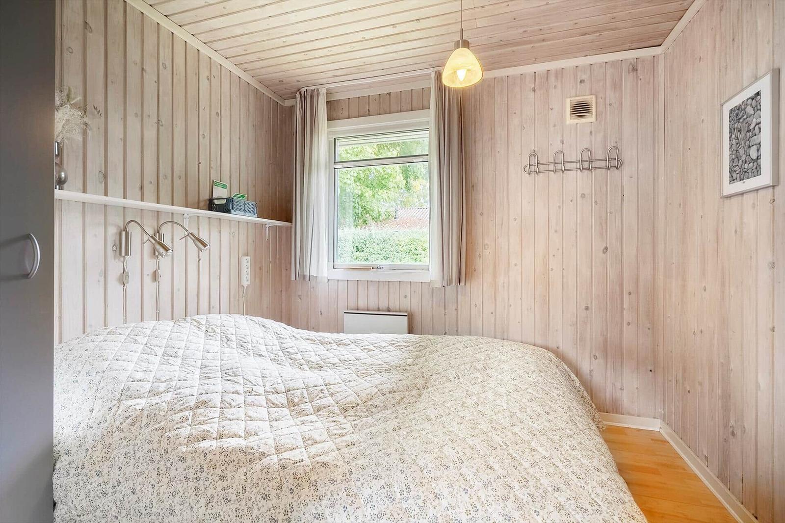 Schlafzimmer mit Holzwand, Bett, Fenster und Hängeregler.