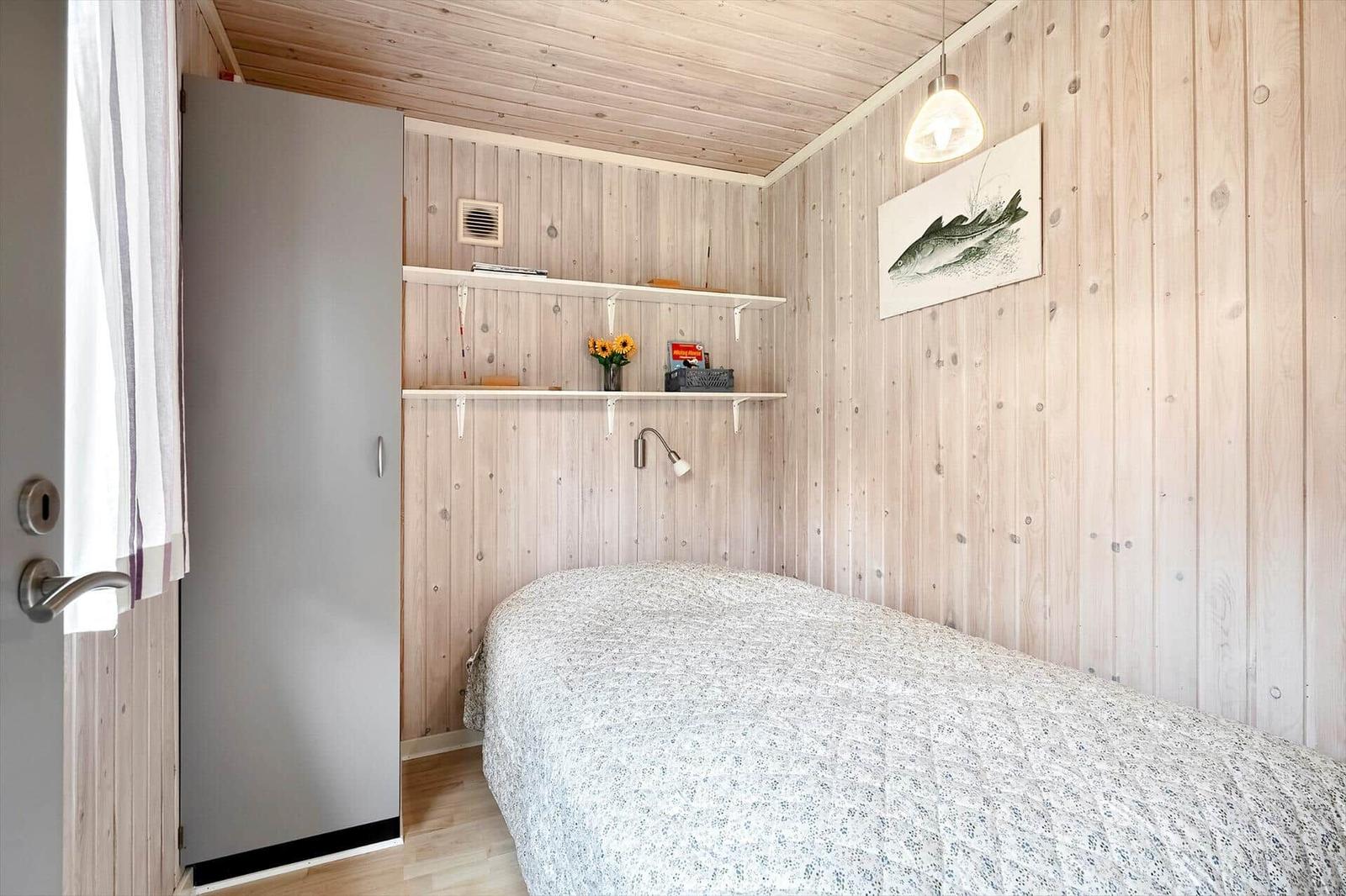 Schlafzimmer mit Holzwand, Bett, Kleiderschrank und Wandbild mit Fisch.