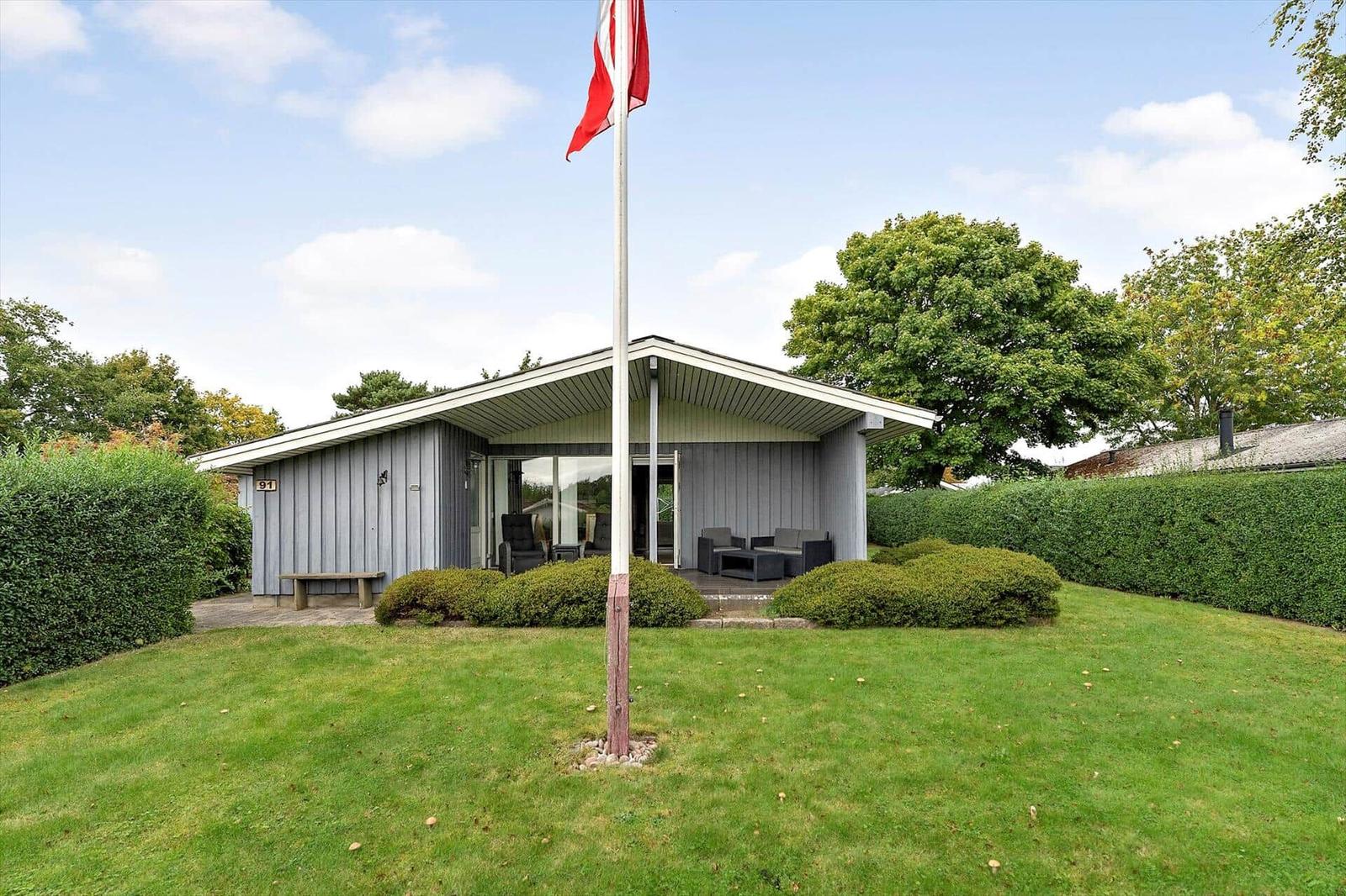 Moderne Villa mit Terrasse, Garten und Flagge. Holzverkleidung und grüne Hecke.