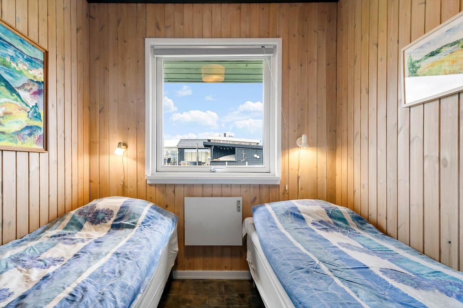 Zwei Betten mit blauen Bettwäschen, Holzwand und Fenster mit Blick auf Haus.