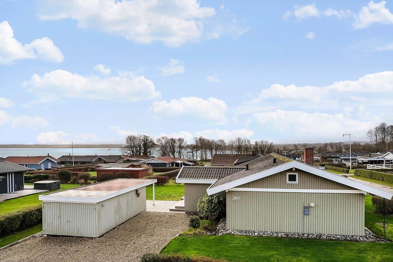 Haus mit Garage und Garten, Blick auf Wasser und Bäume unter blauem Himmel.
