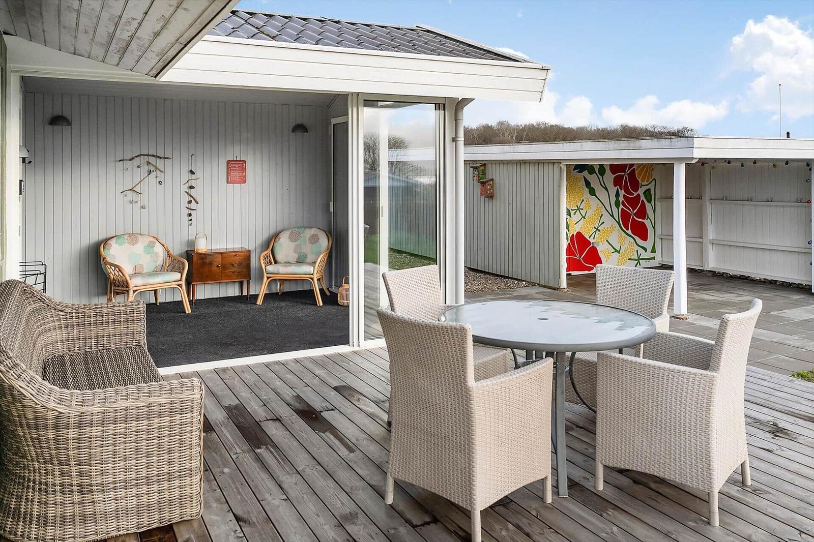 Terrasse mit Sitzgruppe und Tisch. Hintergrund: Wohnbereich mit Stühlen und Wanddekoration.