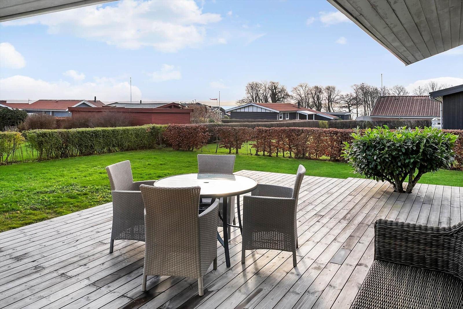 Terrasse mit Tisch und Stühlen, Blick auf grünen Rasen und Hecken.