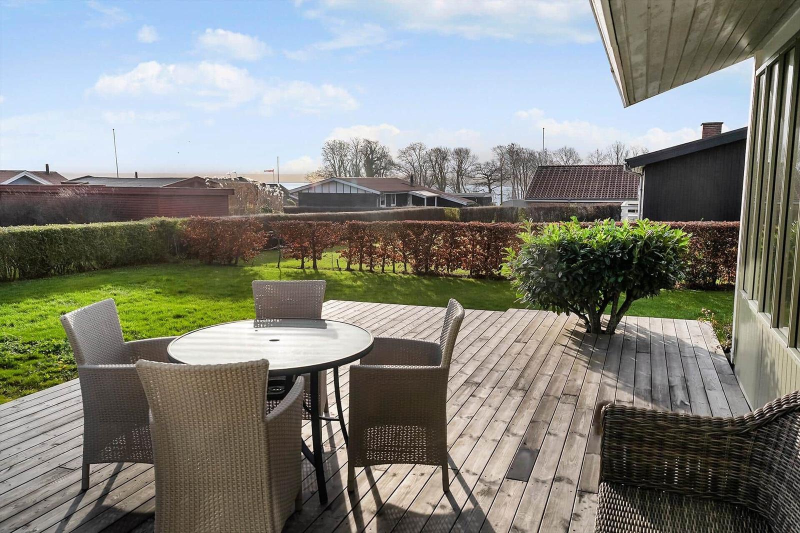 Terrasse mit Tisch und Stühlen, Blick auf Rasen und Hecke.