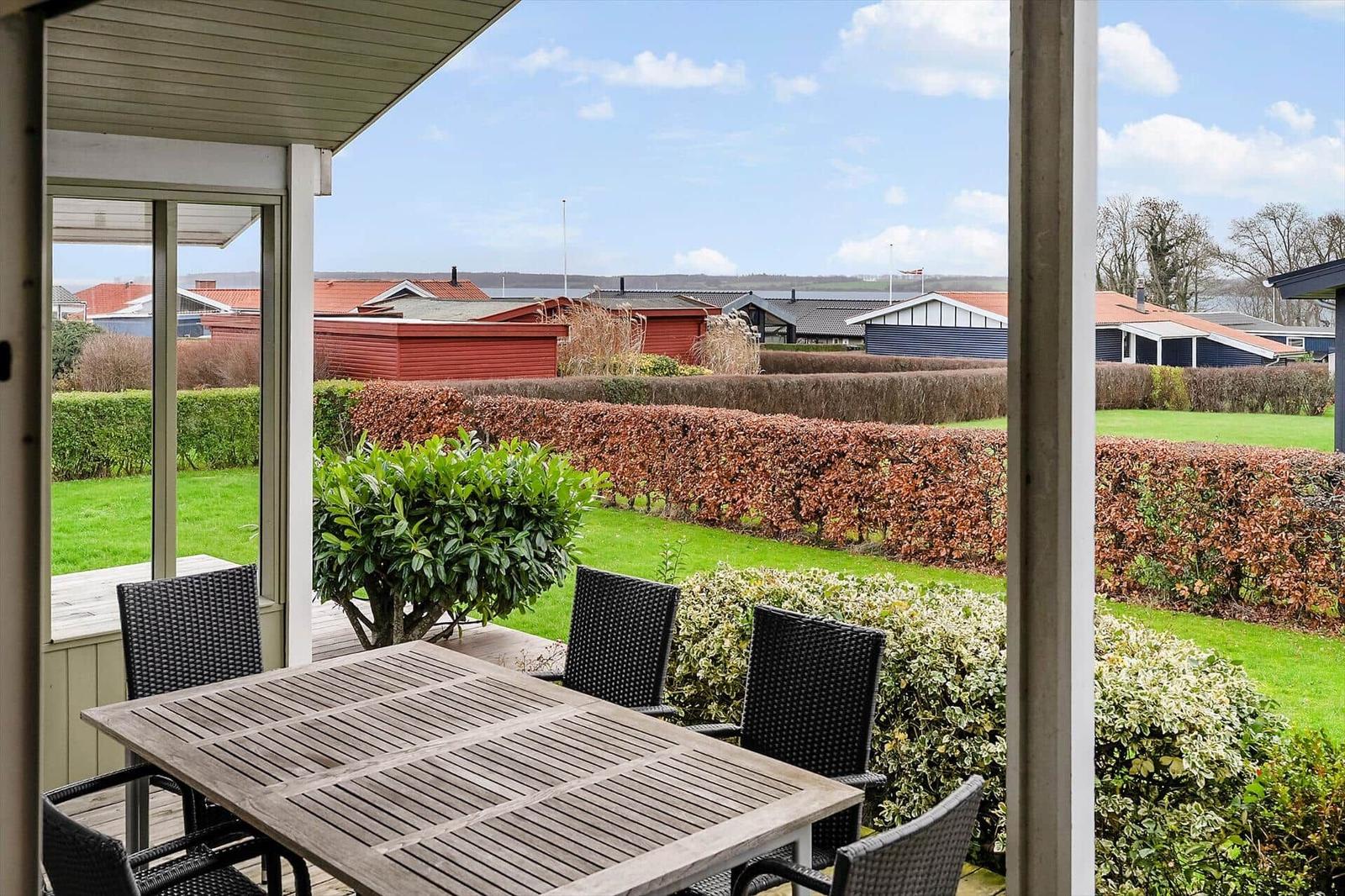 Terrasse mit Tisch und Stühlen, Blick auf Rasen und Hecken.