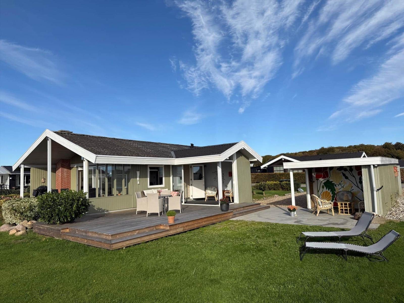 Ein Haus mit Terrasse, Garten und Liegestühlen unter blauem Himmel.