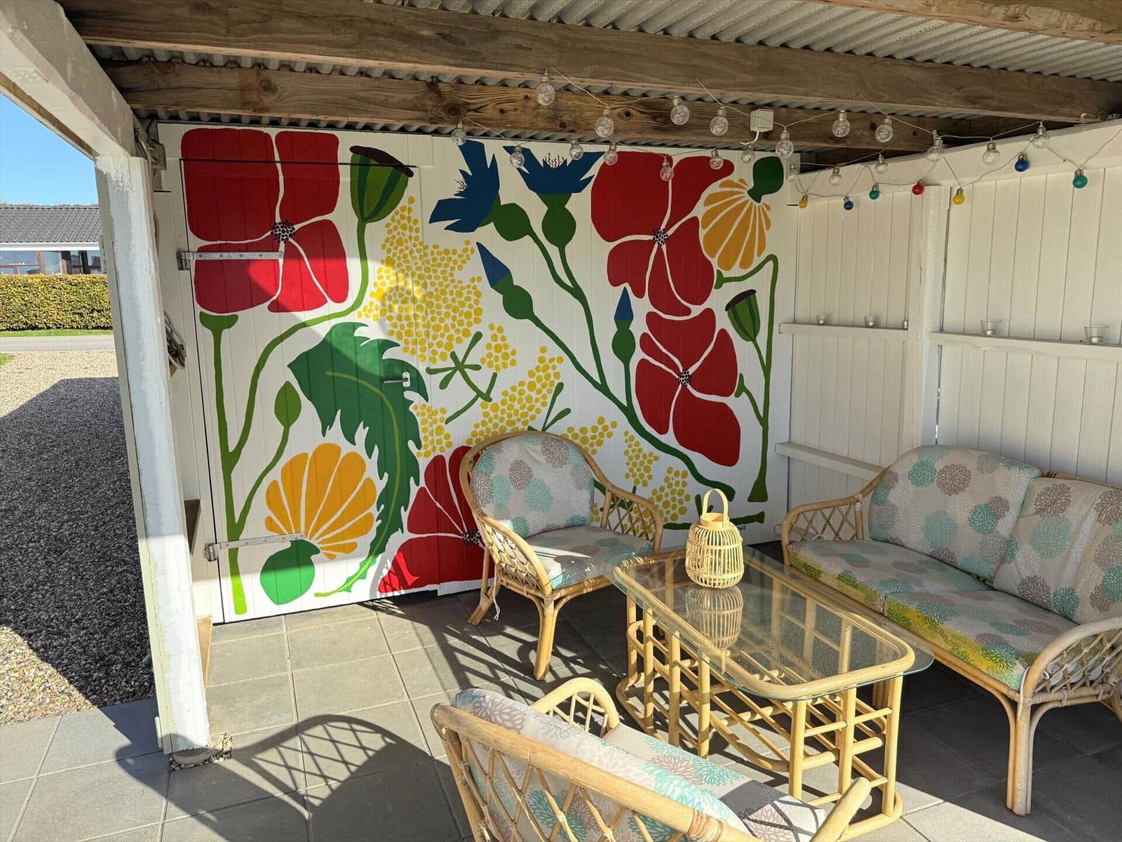 Terrasse mit Rattanmöbeln und farbenfroher Wandmalerei mit Blumenmotiven.