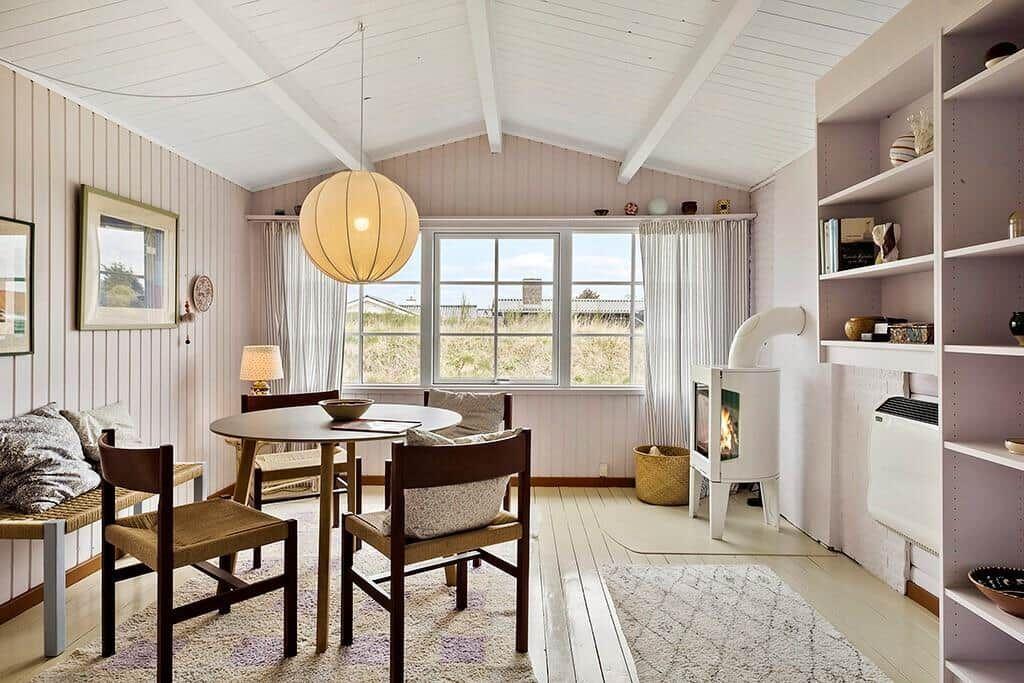 Dining area with table, chairs, and fireplace. Large windows with view outside.