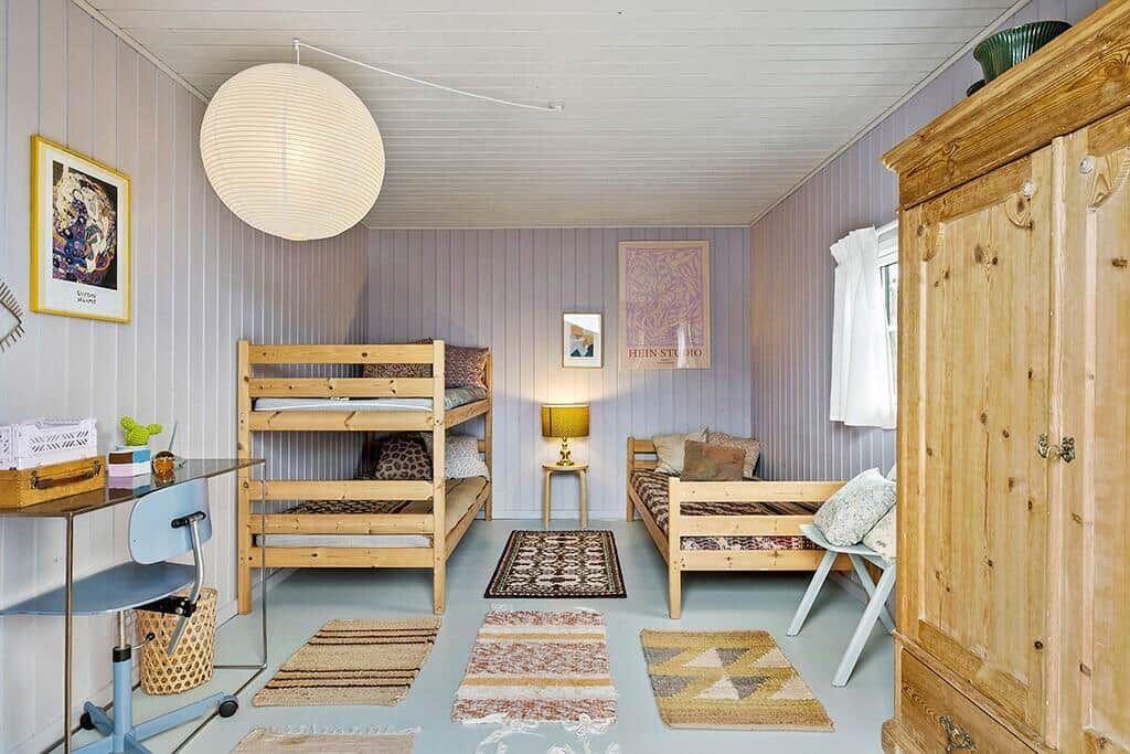 Room with bunk bed, daybed, and wooden wardrobe. Panelled walls and multiple rugs.
