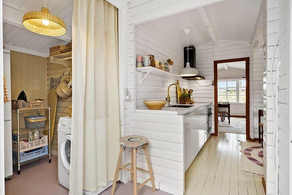 Kitchen with washing machine and shower curtain. Wooden floor and white walls.