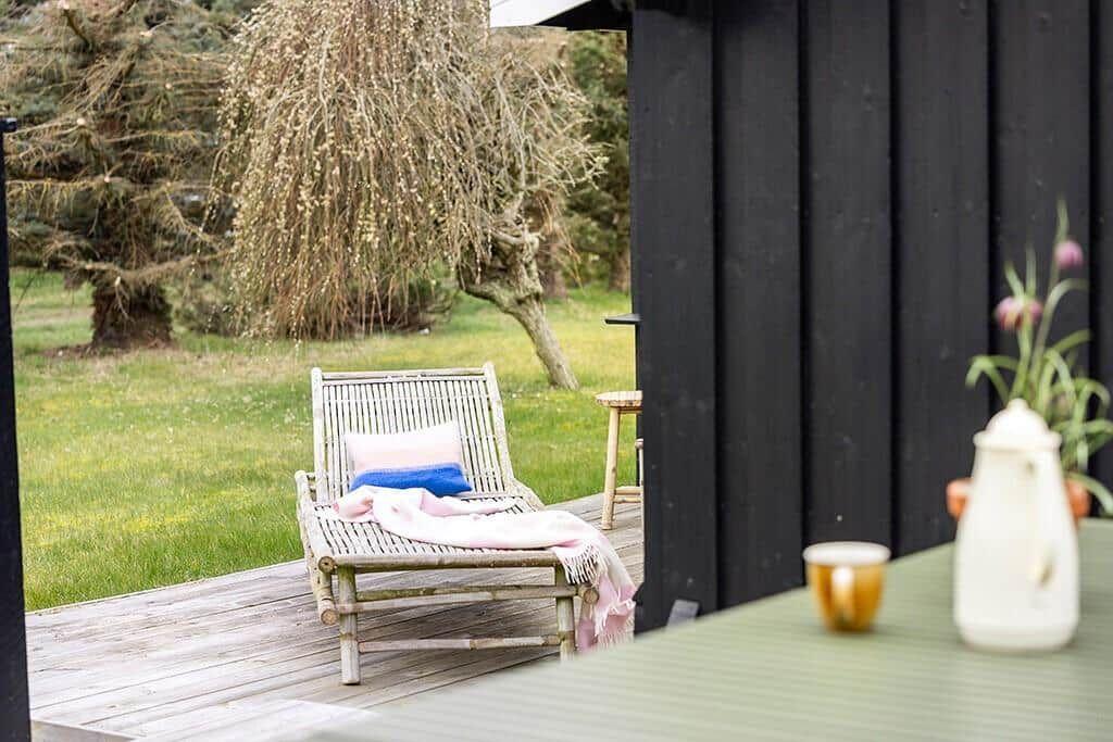 Deck with lounge chair, table, and plants in the garden. Black wooden wall in background.