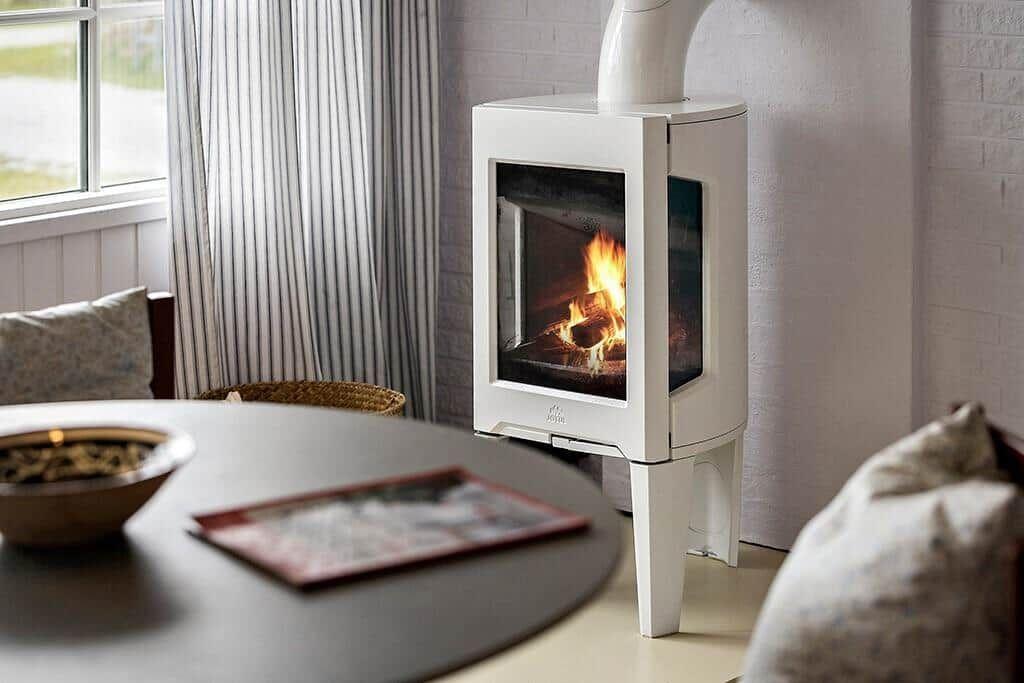 A white wood-burning stove stands next to a round table with chairs.