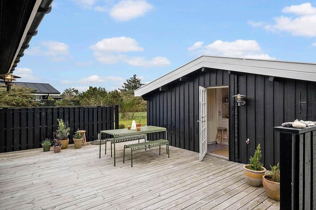 Deck with table and benches in front of black wooden house under blue sky.
