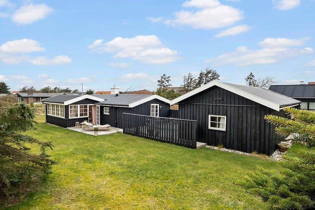 Black wooden house with garden and terrace under blue sky.