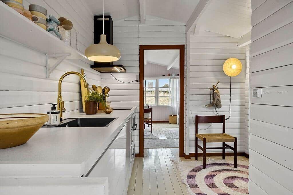 Kitchen with countertop, sink, and gold faucet. Passage to living area with chair and rug.