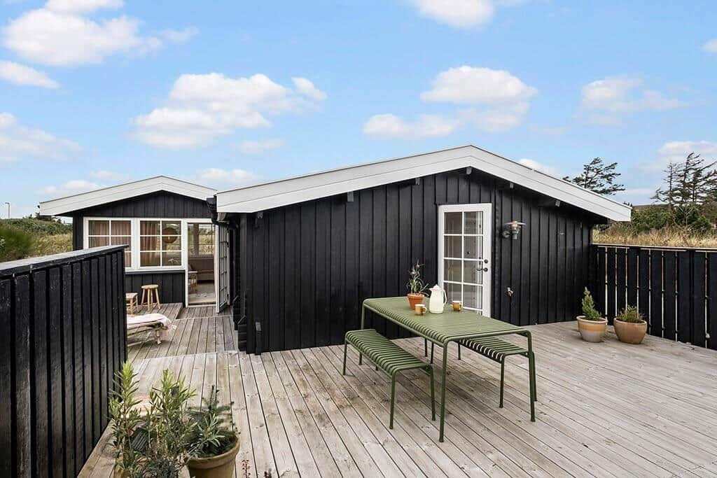 Two black wooden houses with terrace and green table. Background: sky and trees.