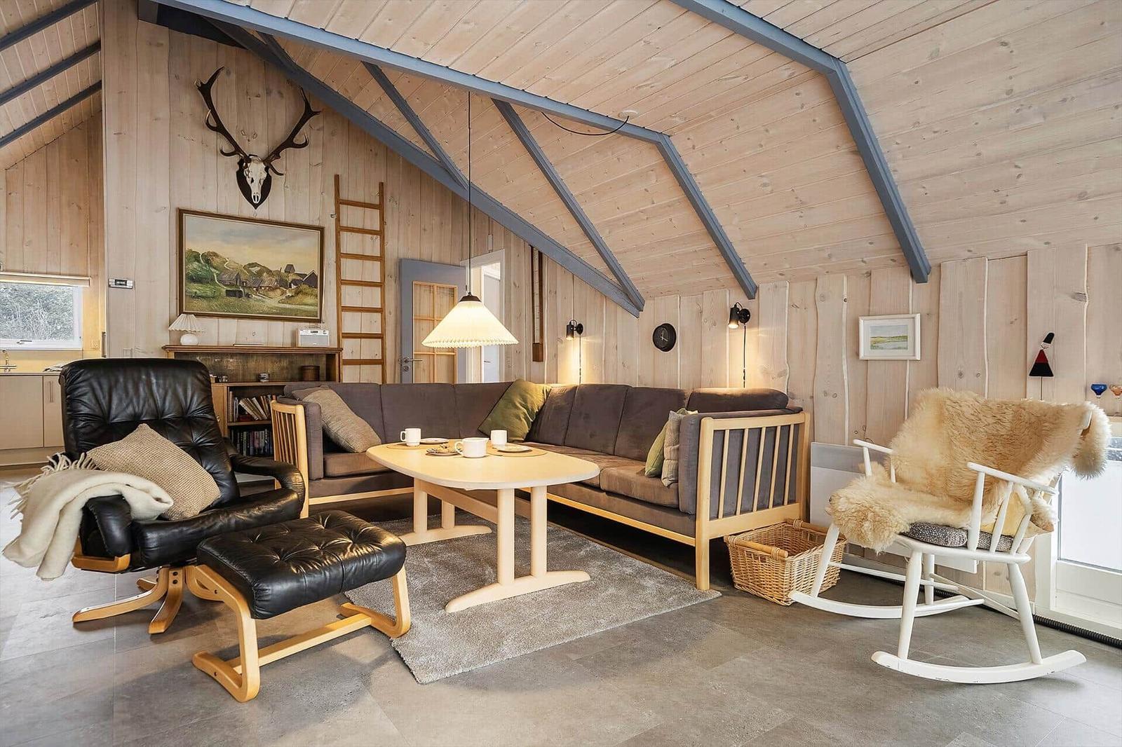 Wohnzimmer mit Holzwand, Sofa, Schaukelstuhl und Hirschgeweih an der Wand.