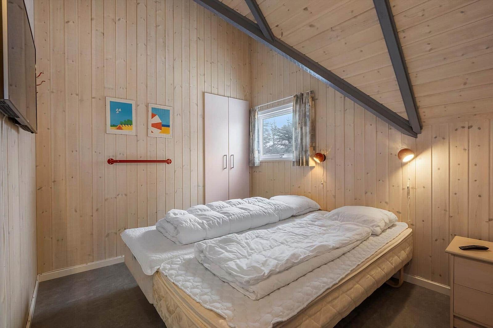 Schlafzimmer mit Bett, Kleiderschrank und Fenster. Holzwände und Deckenbalken.