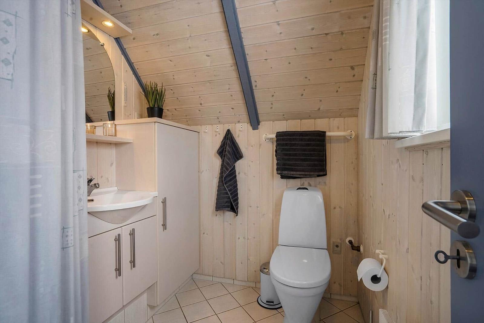 Badezimmer mit Toilette, Waschbecken und Duschvorhang. Holzwände und -decke.