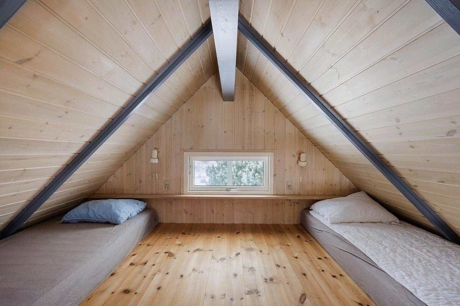 Zwei Betten unter Dachschrägen mit Holzwand und Fenster.